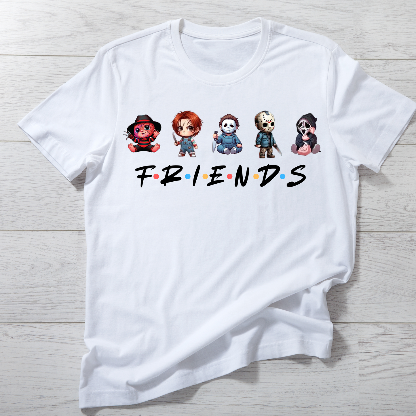 White t-shirt with cartoon character faces and 'FRIENDS' text on a wooden surface
