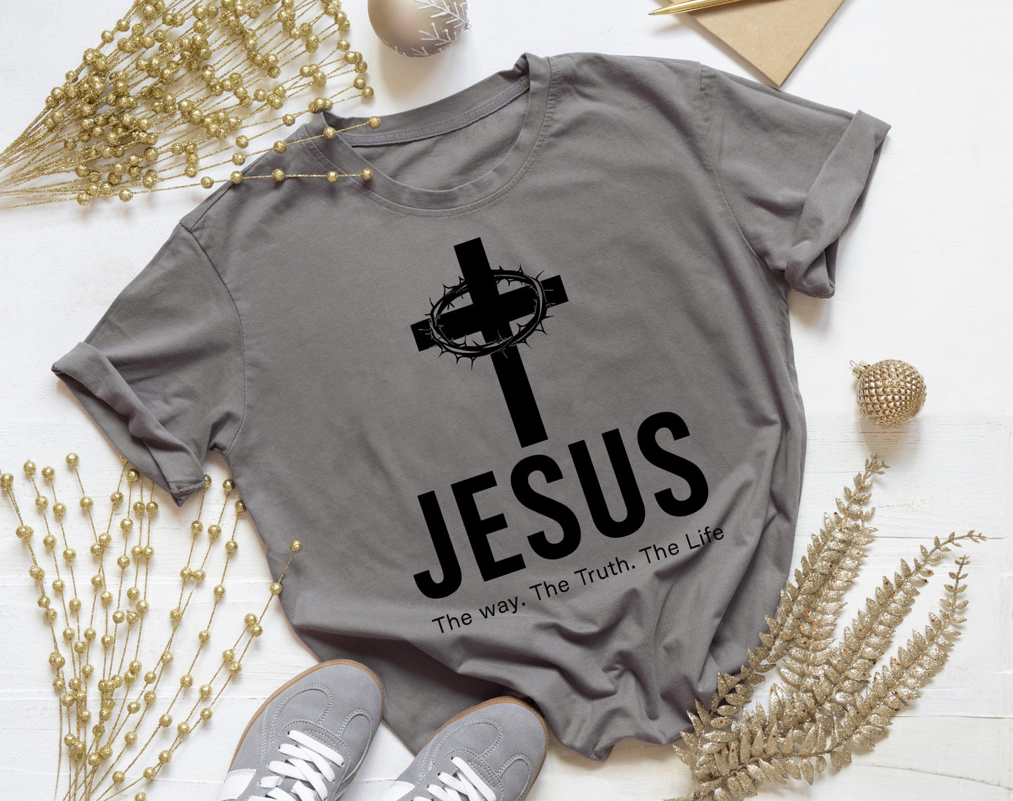 Gray t-shirt with 'Jesus' and cross design on a white surface with decorative elements.