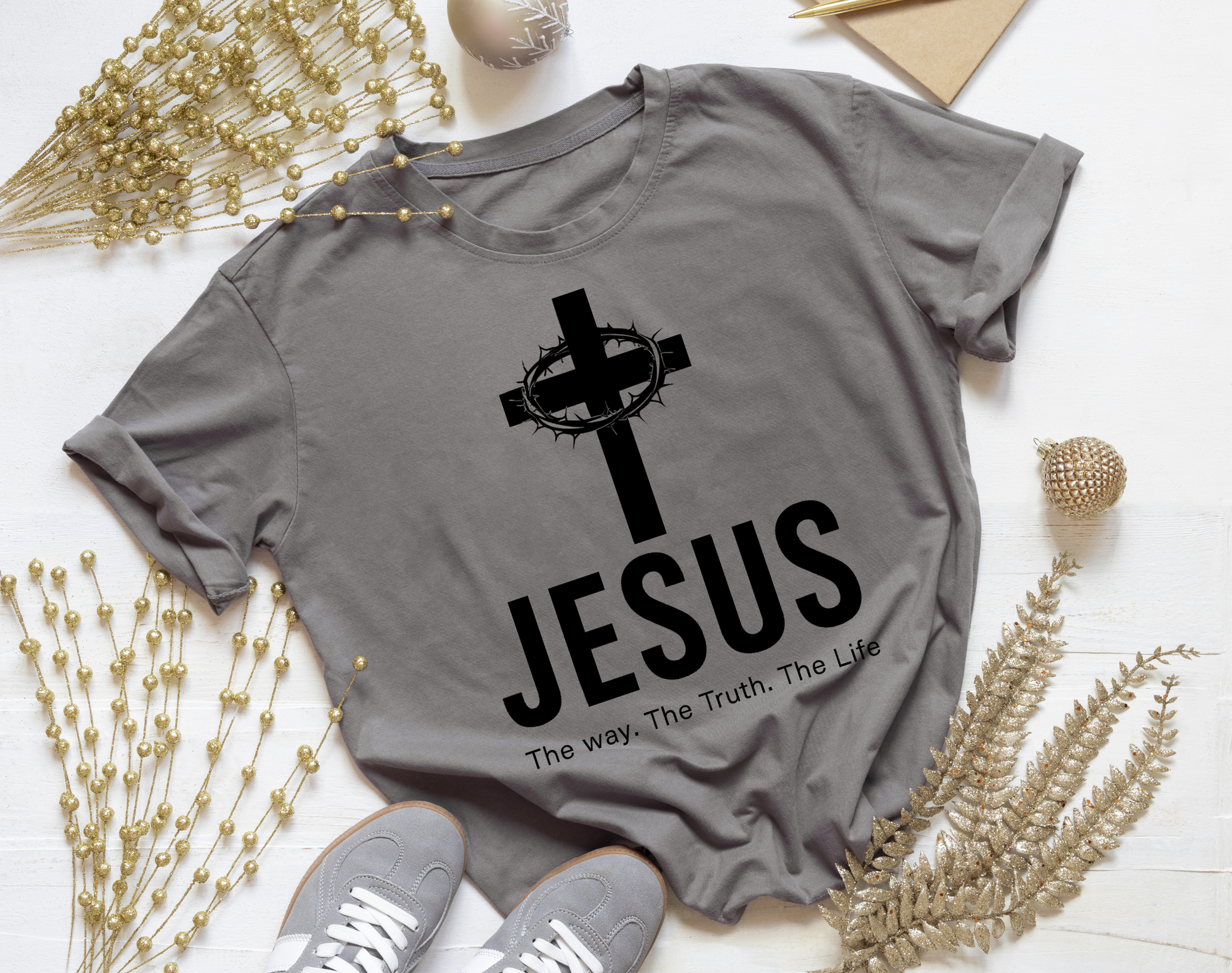 Gray t-shirt with 'Jesus' and cross design on a white surface with decorative elements.