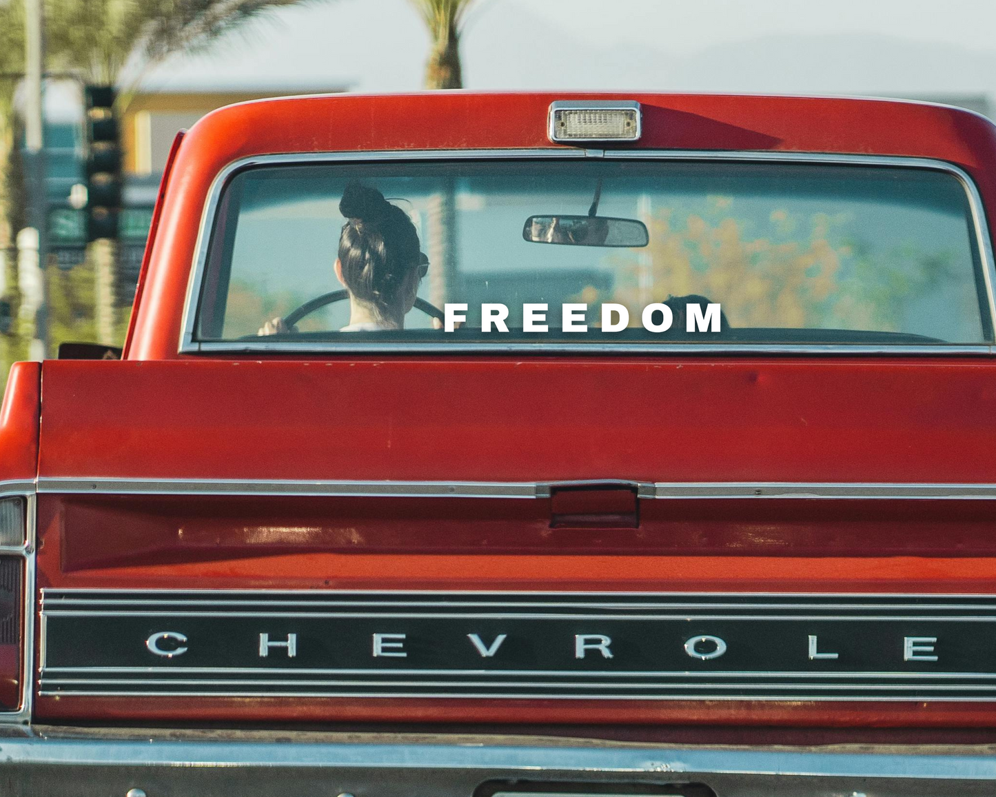Matte White Vinyl Decal that Says Freedom in reference to Charlie Kirk on the rear window of a red old style chevrolet truck. 