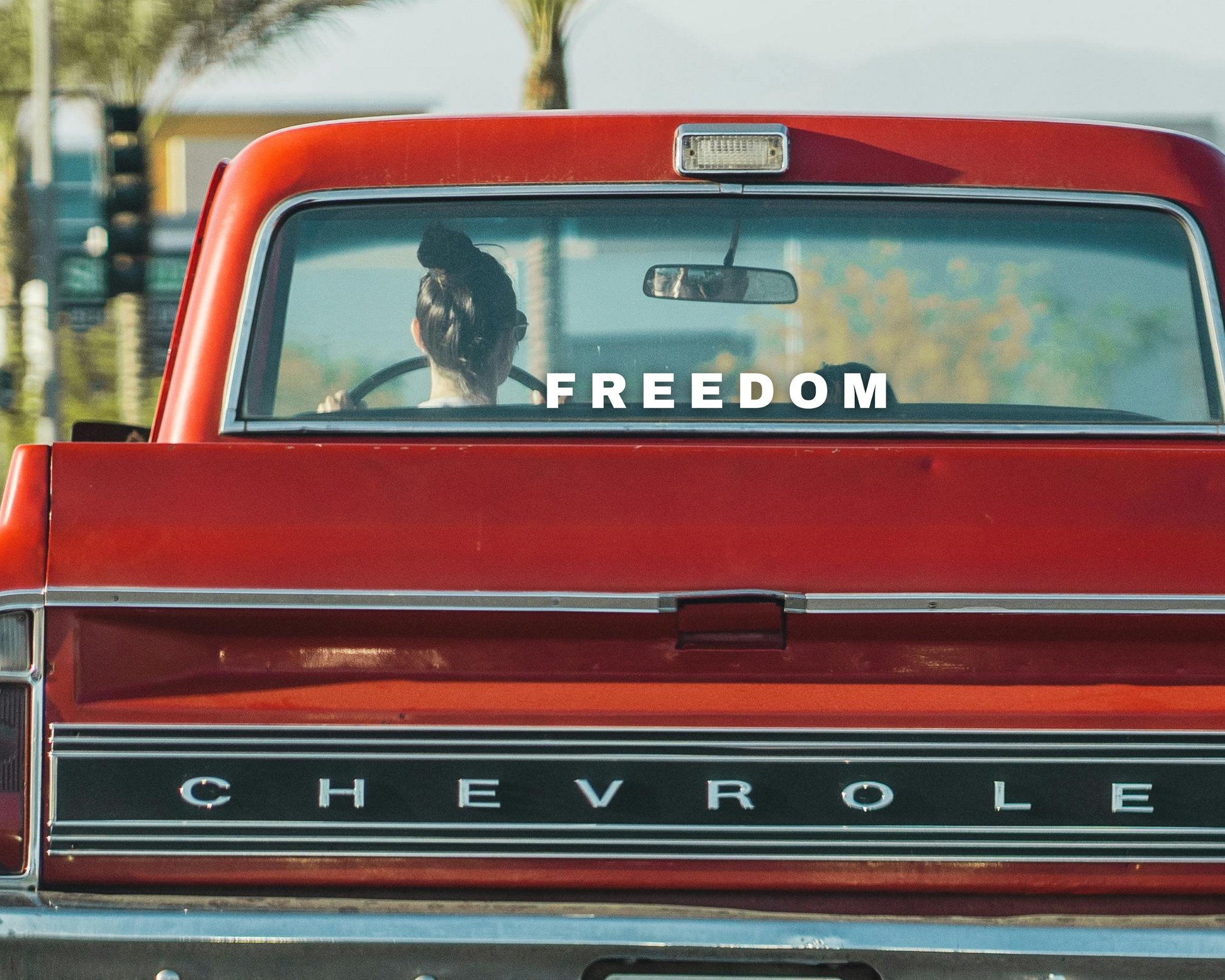 Matte White Vinyl Decal that Says Freedom in reference to Charlie Kirk on the rear window of a red old style chevrolet truck. 