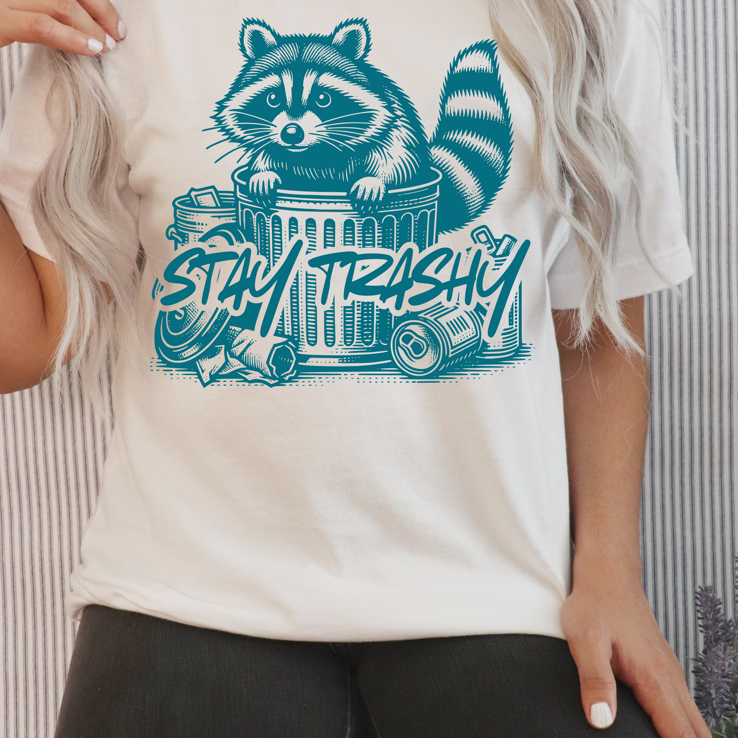 White shirt with the saying stay trashy and racoon coming out of a trash can. 