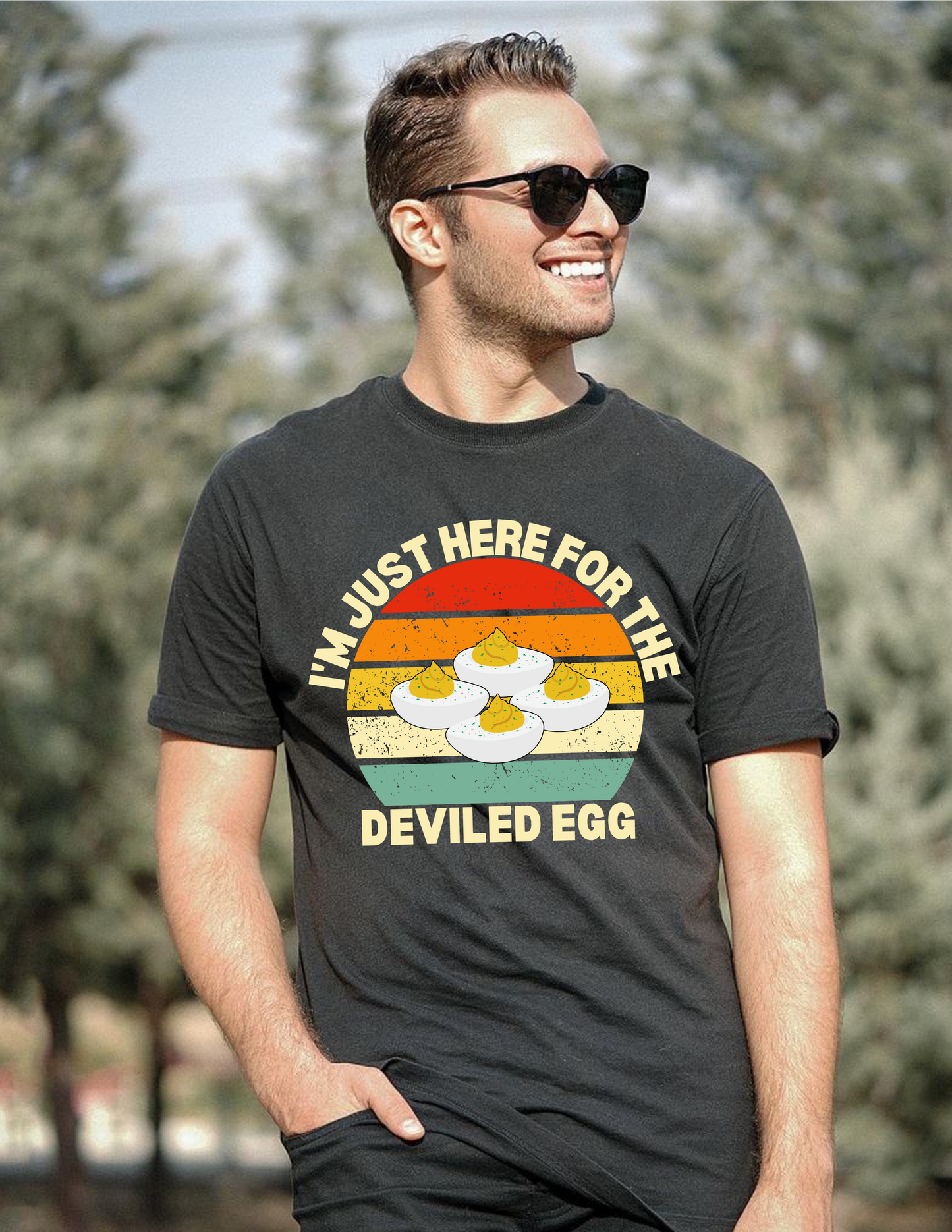 Man wearing sunglasses and a black t-shirt with a graphic and text outdoors.