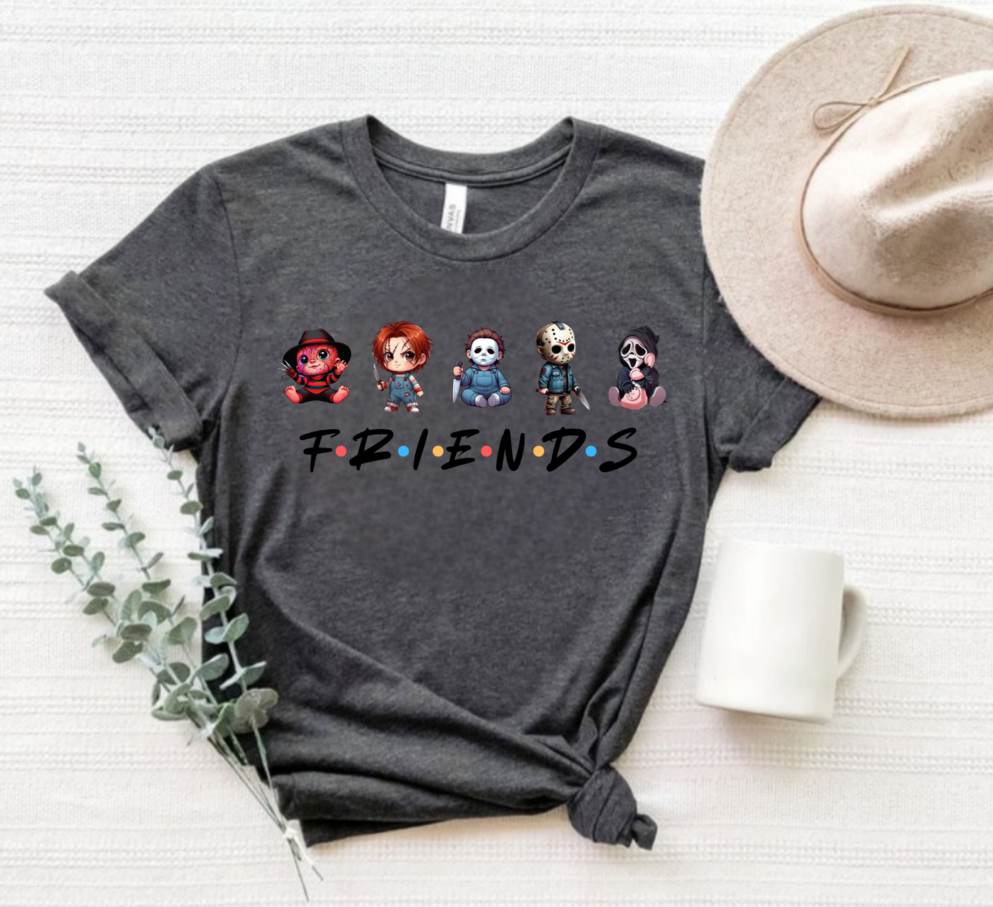 Gray t-shirt with cartoon character design and 'FRIENDS' text, placed on a white surface with a hat and plant.