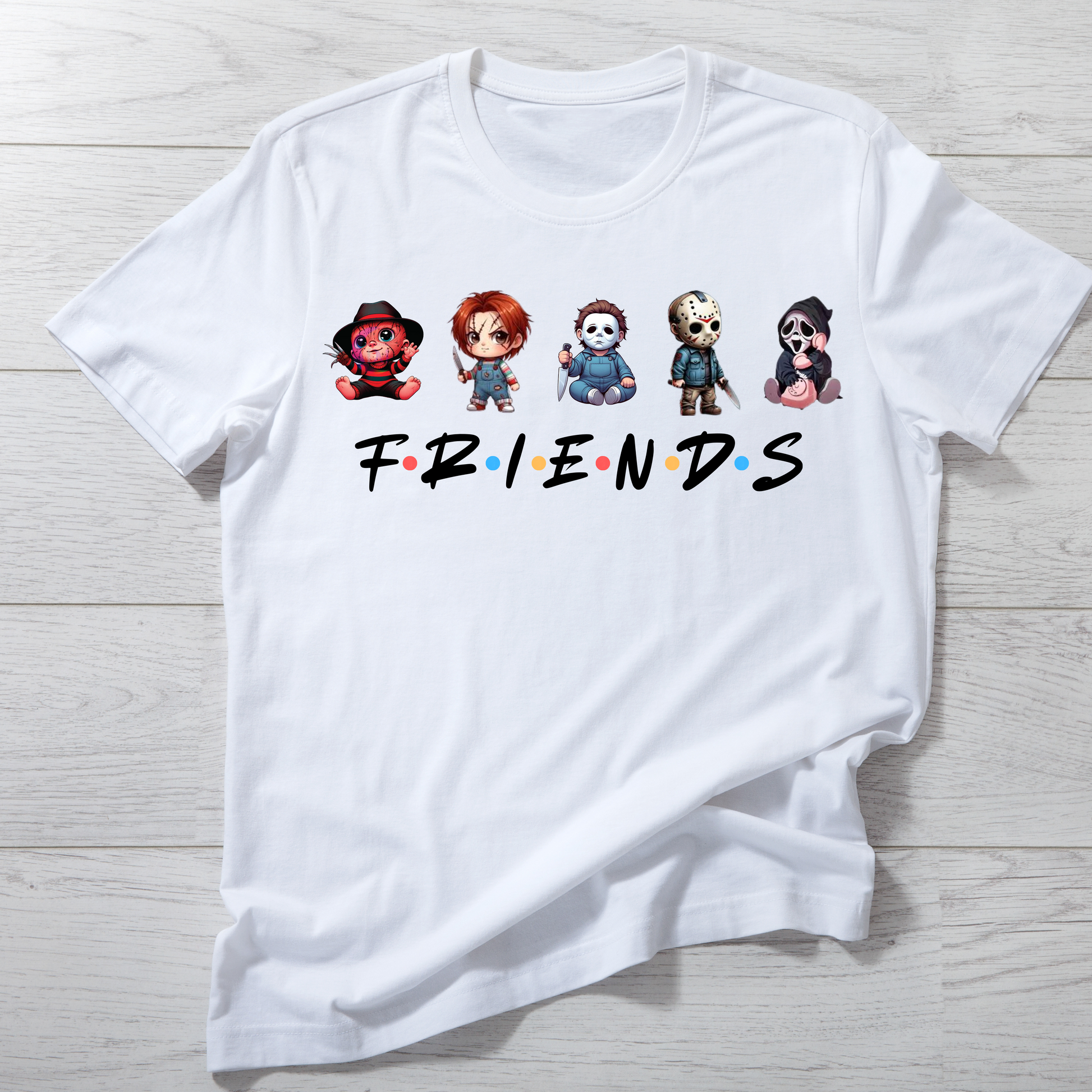 White t-shirt with cartoon character faces and 'FRIENDS' text on a wooden surface