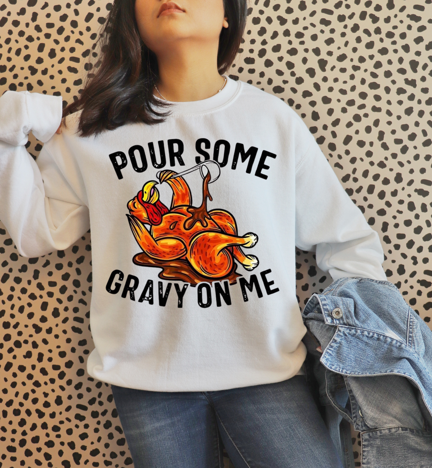 Person wearing a white sweatshirt with a graphic design and text against a patterned wall.