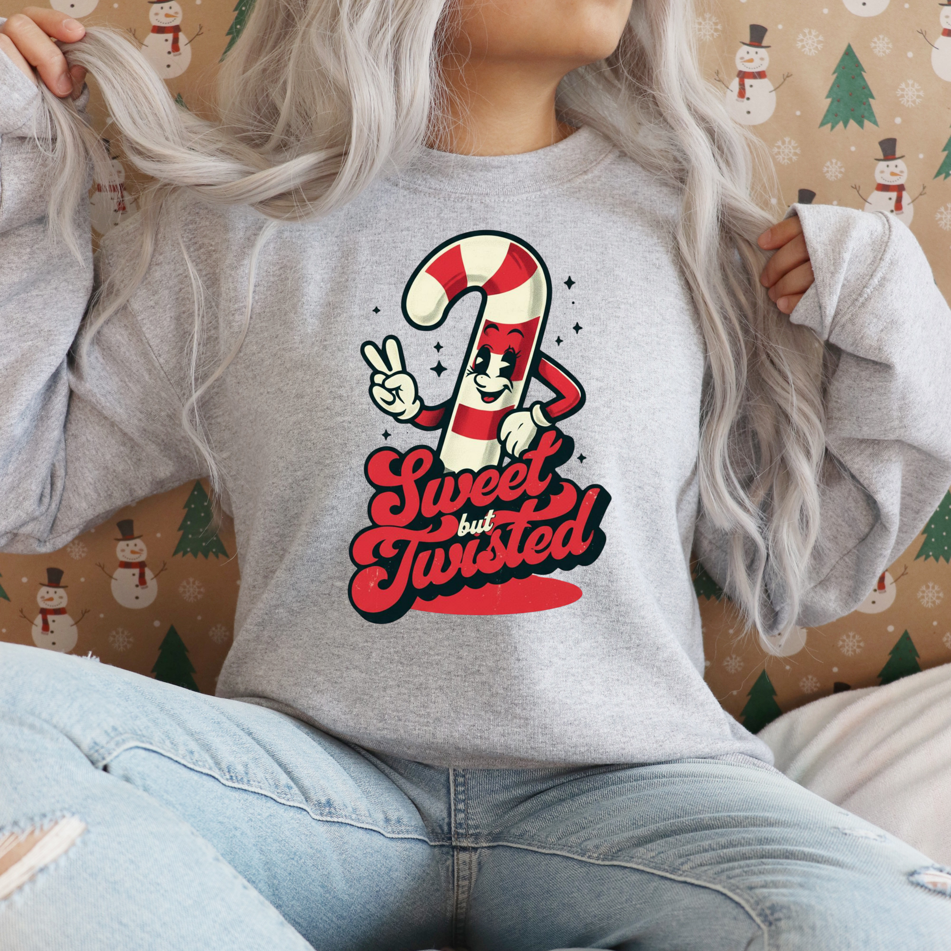 Person wearing a gray sweatshirt with a candy cane graphic design and 'Sweet but Twisted' text, sitting against a festive background.